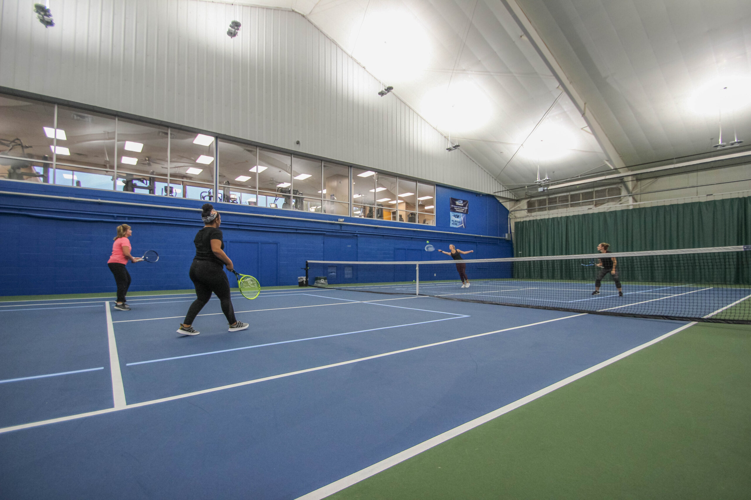 Four women playing doubles tennis at Parkside Fitness